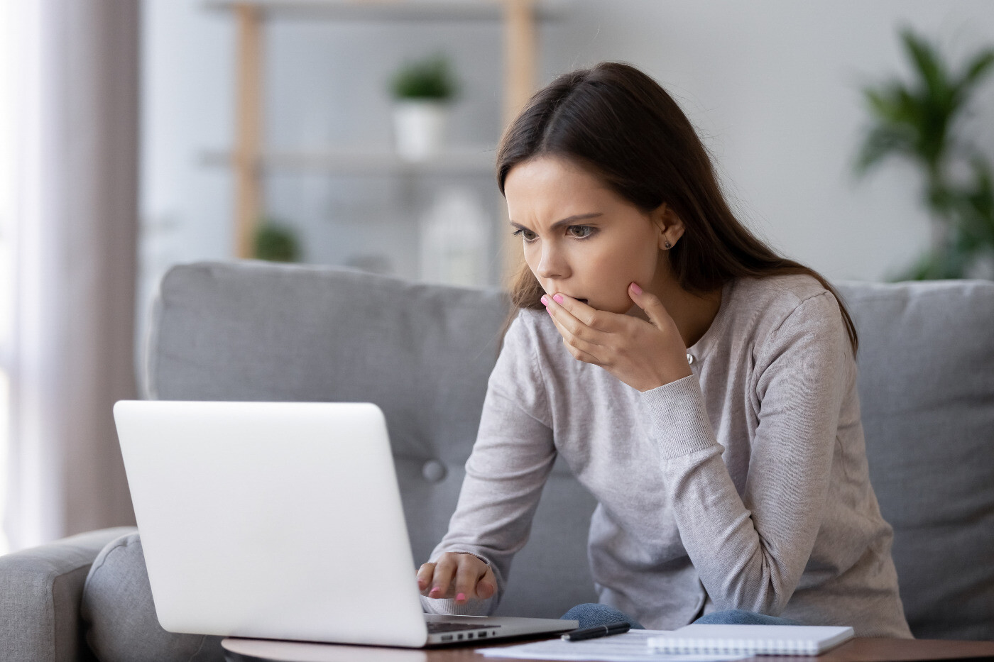 Woman with shoulder-length brunette hair staring in shock at her laptop screen due to SEO or digital marketing scam