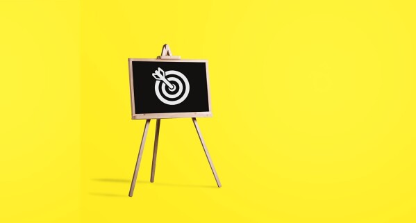Chalkboard displaying bull's eye on easel in front of yellow background, representing reaching a targeted goal 