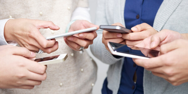 Multiple people standing in a huddle using social media on their mobile devices