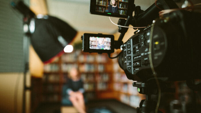 Video camera filming person in background doing interview