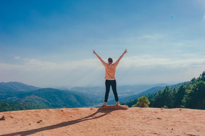 Woman standing with back turned and hands in air facing landscape scene