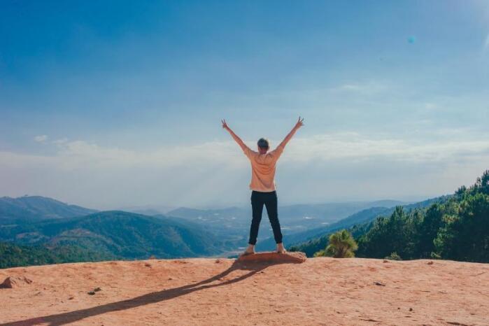 Woman standing with back turned and hands in air facing landscape scene