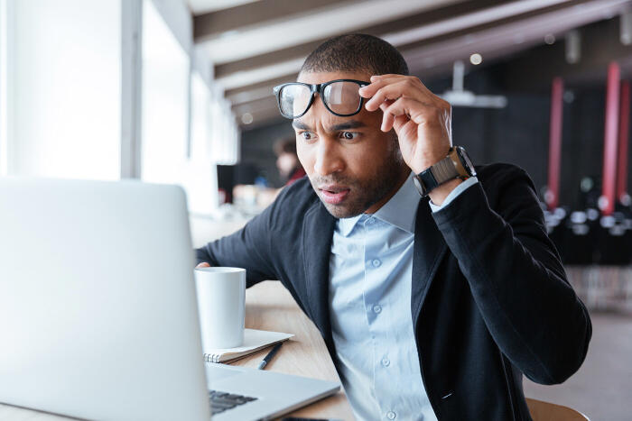 Man lifting up his glasses staring in shock at his laptop due to a website crash